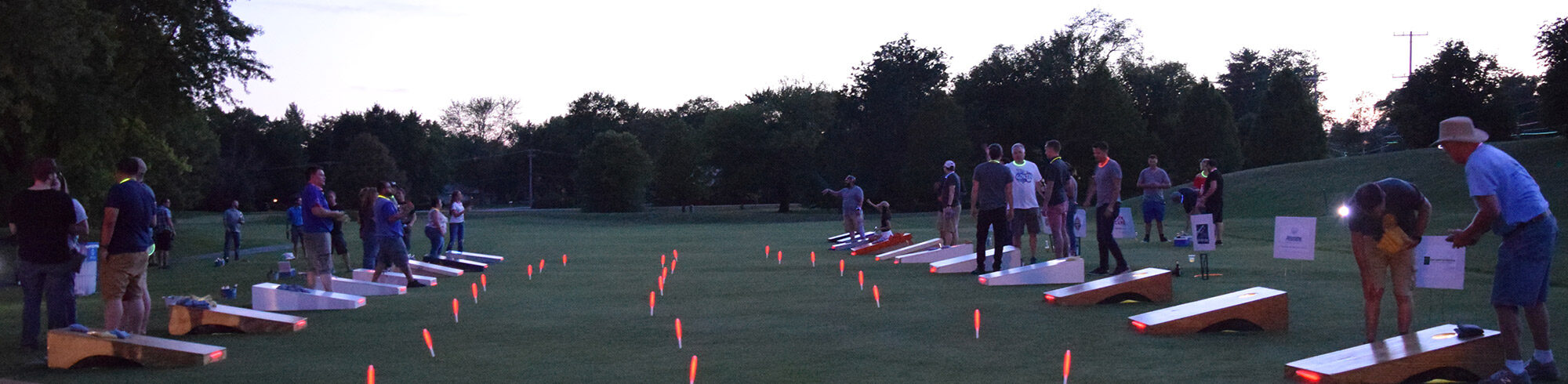 people playing bags at night with glow stick illumination